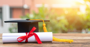 high school diploma sobre uma mesa ao lado de um chapéu de formatura, representando a conclusão do ensino médio internacional