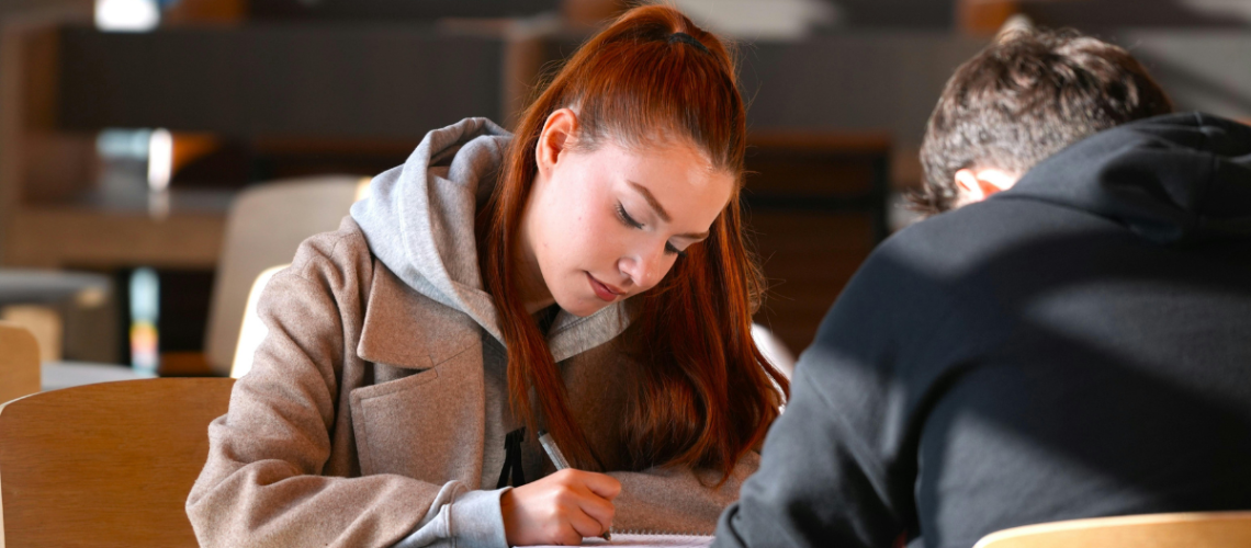 aluna estudando em biblioteca com material didático do sistema